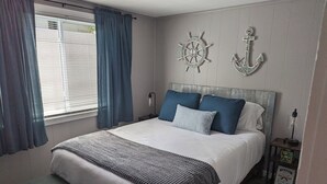 Ein Schlafzimmer mit einem Bett, einem Nachttisch, einer Lampe, Vorhängen und Wanddekoration im Seestil.