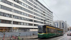 Een tram rijdt over rails, een gebouw met veel ramen, en een fiets geparkeerd in de buurt van de tram.