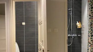 A bathroom with a toilet, a shower with a handheld showerhead, and a towel rack. - Homely 1BR in Lively Area with Strategic Location (Helsinki)