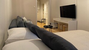 A modern hotel room with a bed, a sofa, a desk with a TV, and a small table. - Homely 1BR in Lively Area with Strategic Location (Helsinki)