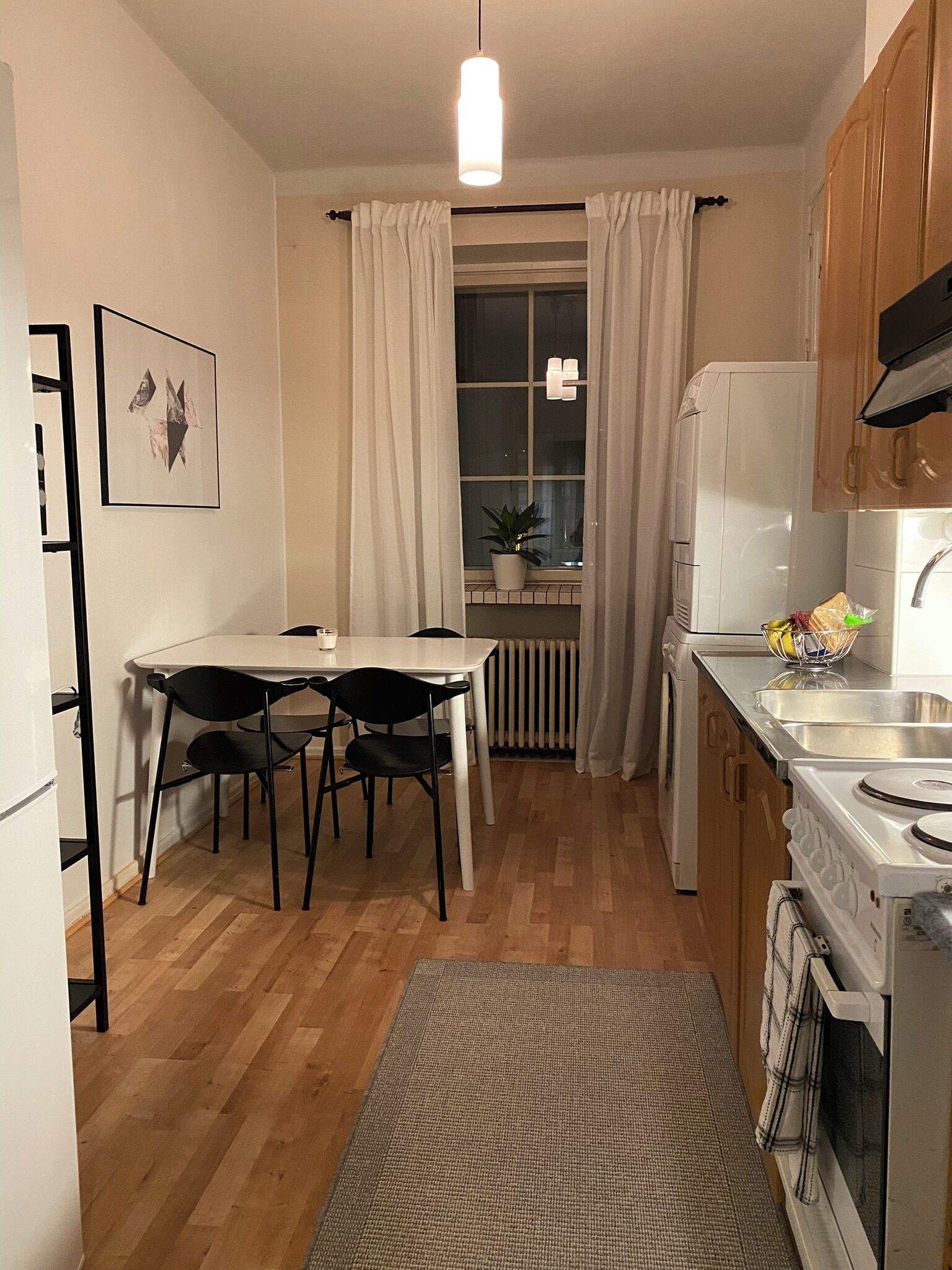 A compact kitchen with a dining table, chairs, a refrigerator, a stove, and a window with curtains.
