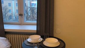 Una habitación pequeña con ventana, un reloj de pared, una mesa con dos sillas y una cama.