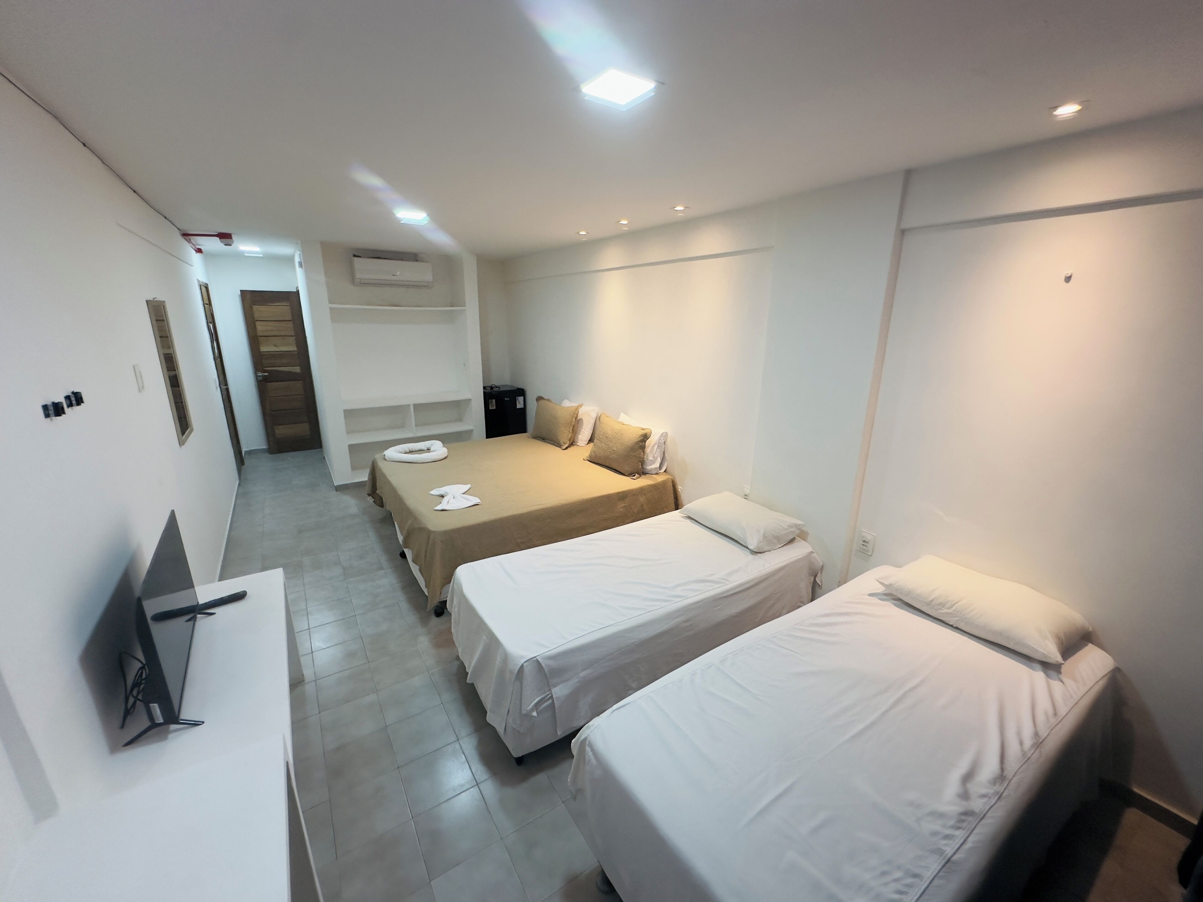 Quarto de hotel moderno com duas camas, uma escrivaninha e um guarda-roupa embutido.
