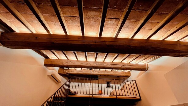 Eine Treppe mit Holzbalkendecke, einem schwarzen Geländer und einer Tür am Fuß.