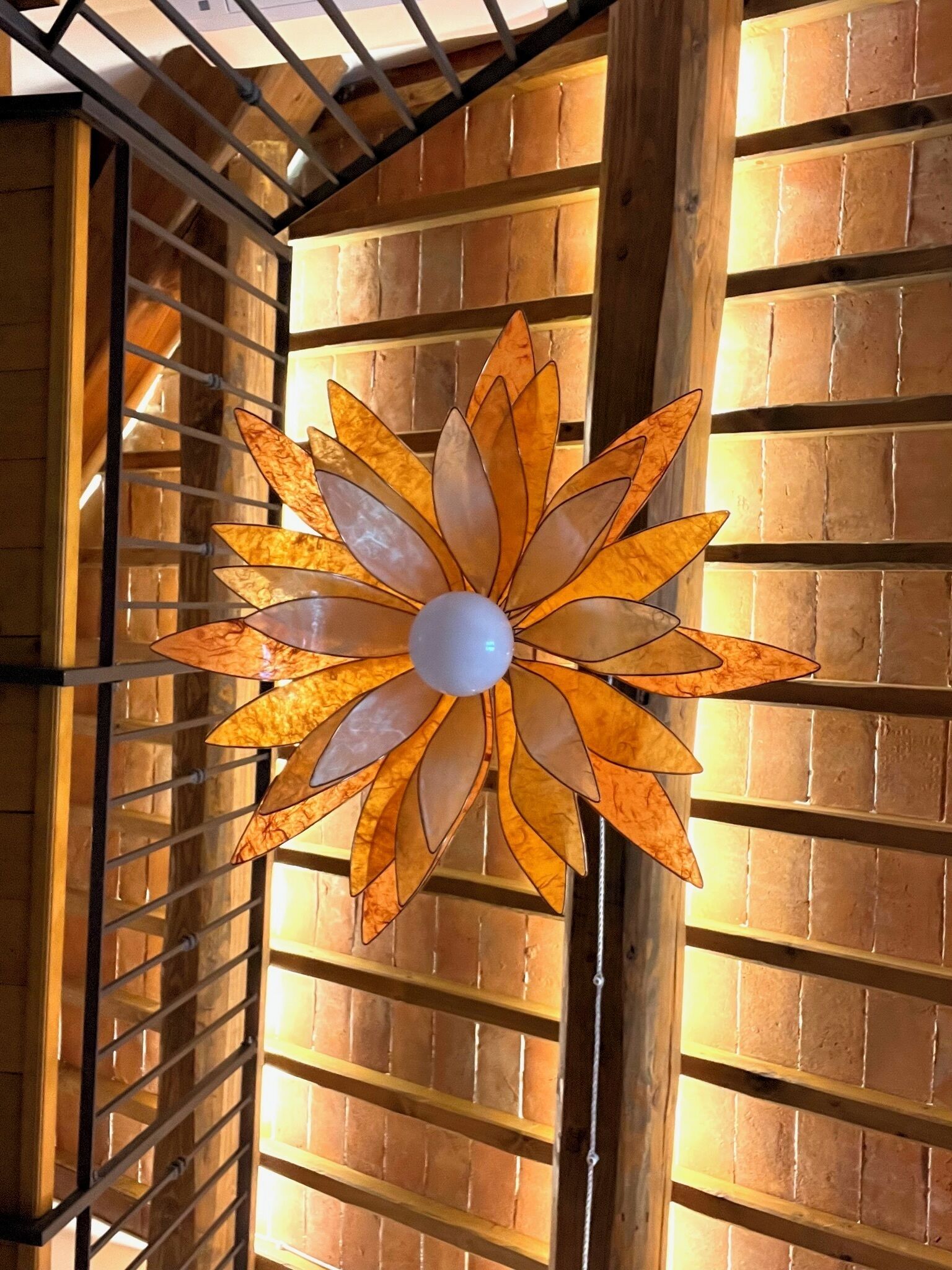 Un ventilador de sostre amb un disseny floral, penjant d'una estructura metàl·lica en una habitació amb bigues de fusta i parets de maó.