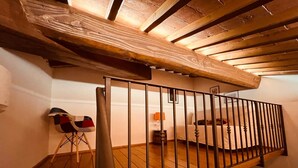 Eine Holztreppe mit Metallgeländer führt zu einem Schlafzimmer mit Bett und Nachttisch.