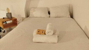 A neatly made bed with white linens, two rolled towels, and a small wooden nightstand with a lamp. - Stylish and modern Studio in Pigalle (Paris)