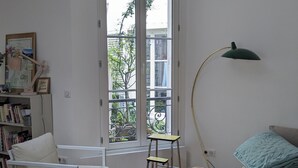 A room with a white chair, a sofa, a standing desk, and a floor lamp. - Stylish and modern Studio in Pigalle (Paris)