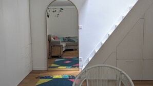 A room with a white wicker chair, a colorful rug, and a staircase leading to another room. - Stylish and modern Studio in Pigalle (Paris)