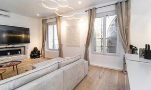 A modern living room with a sofa, a flat-screen TV, a coffee machine, and a window with curtains.