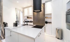 A modern kitchen with a central island, white cabinetry, and a black range hood.