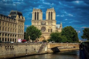A historic cathedral with two prominent towers, a large rose window, and a river in the foreground.