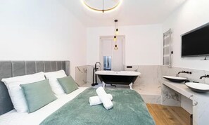 Une chambre à coucher moderne avec un lit, un plaid vert et une salle de bain équipée d’une baignoire, d’un lavabo et d’un miroir.