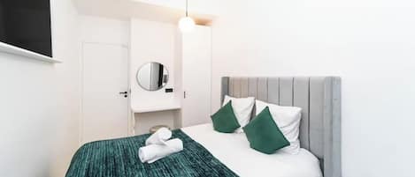 A hotel room with a bed, a mirror, a bedside table, and a lamp.