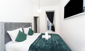 Ein Hotelzimmer mit einem Bett, Kissen, einer Decke, einem Fenster mit Vorhängen und einer Pendelleuchte.