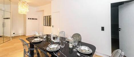 Un comedor con una mesa larga preparada para cuatro personas, sillas traslúcidas y una lámpara de techo moderna.