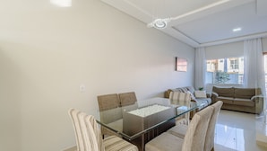 Een moderne woonkamer met een glazen eettafel, gestreepte stoelen, een bank en een groot raam met gordijnen.