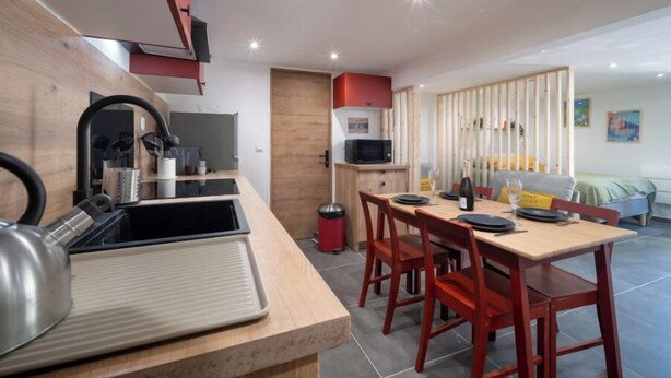 A compact kitchen with a microwave, sink, and modern appliances. There is a dining area with a wooden table and red chairs.