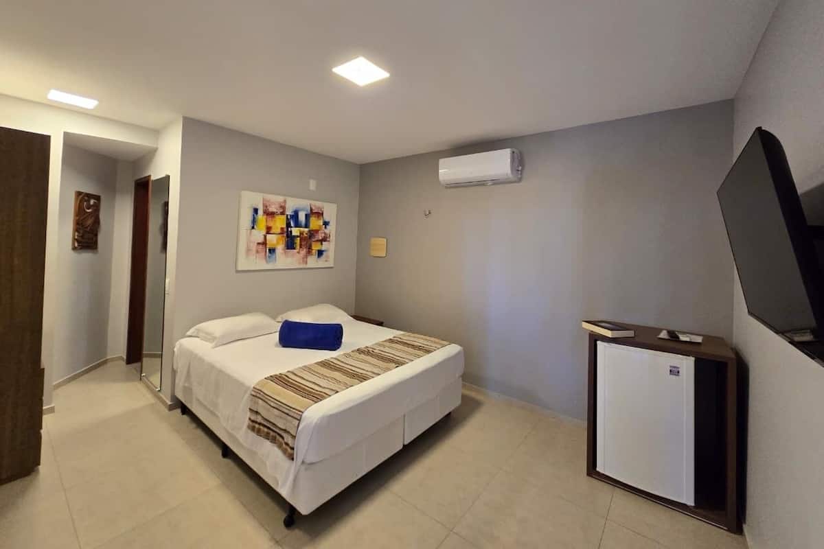 A hotel room with a bed, a small desk, a television, and an air conditioning unit.