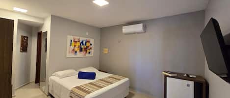 A hotel room with a bed, a small desk, a television, and an air conditioning unit.
