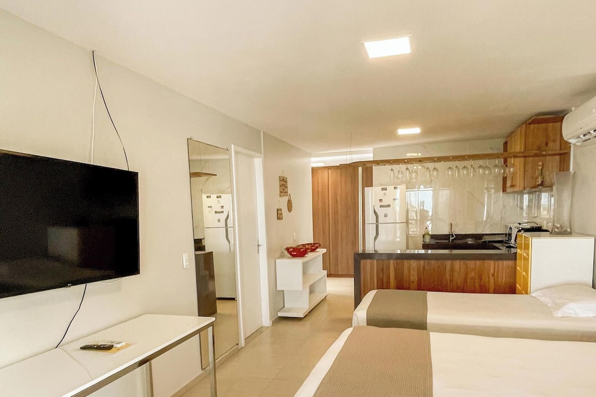 A hotel room with a TV, a desk, a bed, and a kitchenette.