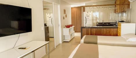 A hotel room with a TV, a desk, a bed, and a kitchenette.
