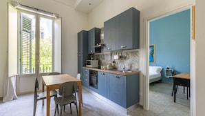 Eine kompakte Küche mit modernen Geräten, ein Essbereich mit Tisch und Stühlen sowie ein Schlafzimmer mit Bett und Nachttisch.