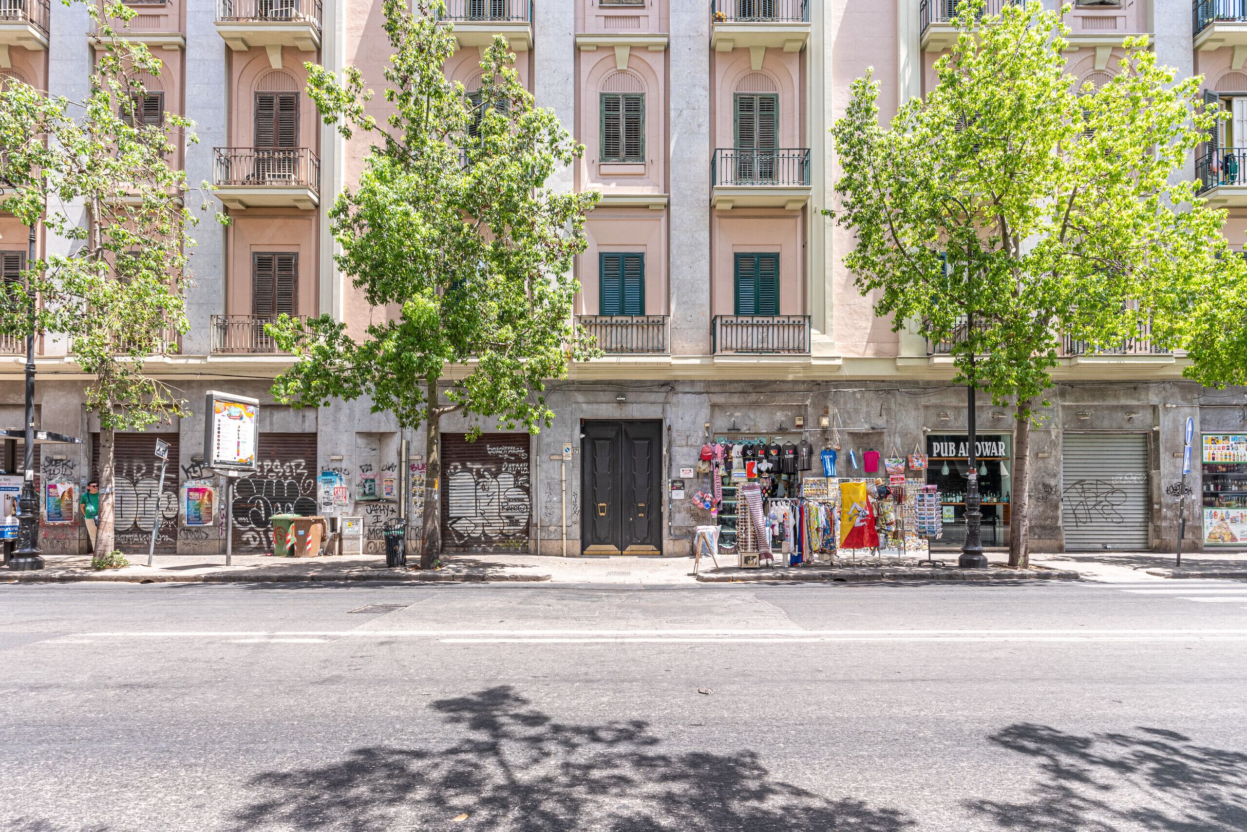 A street view with a row of buildings, some with balconies, and a storefront with various items on display.