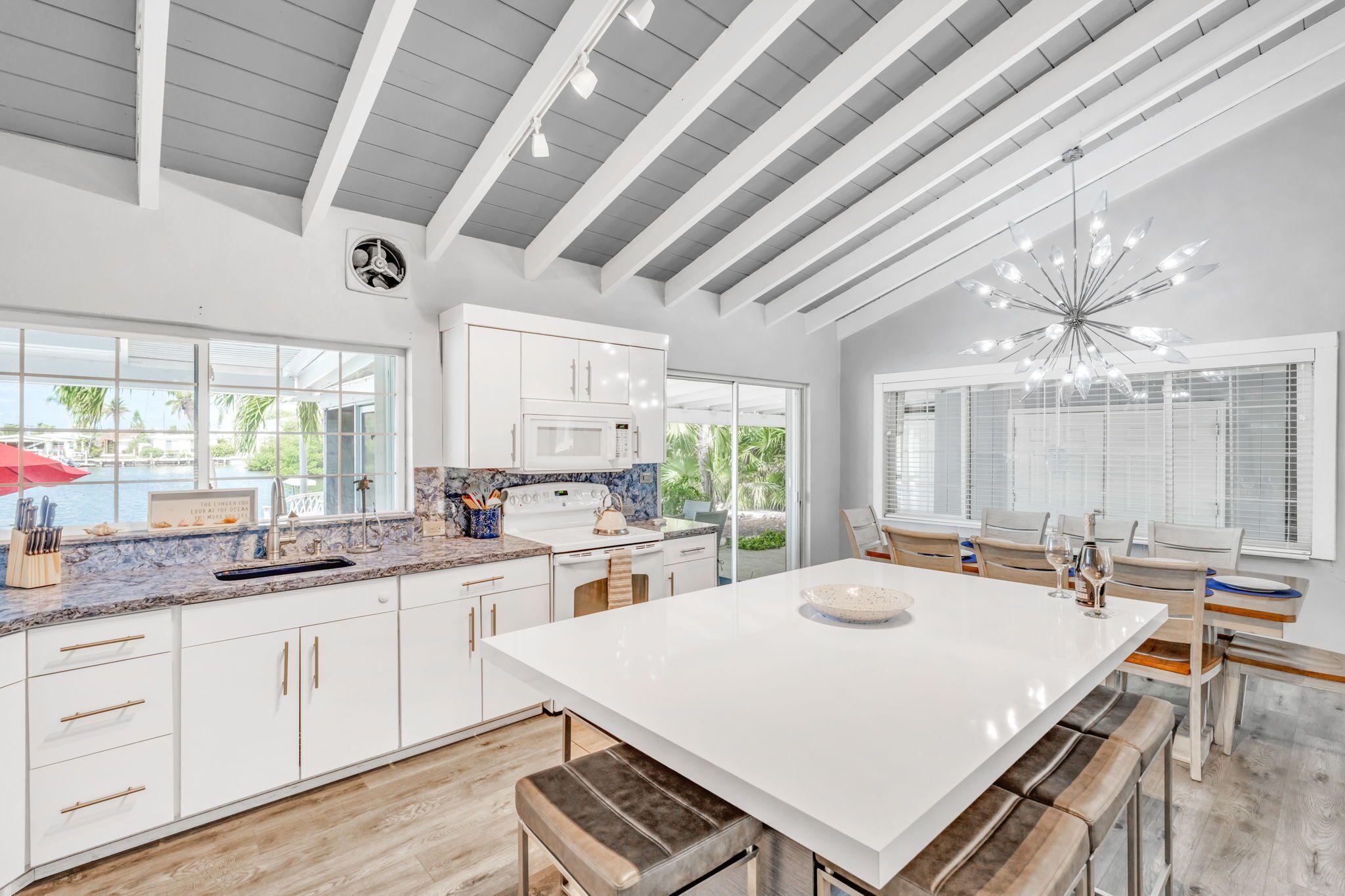 A modern kitchen with white cabinets, a large island, and a dining area with wooden chairs.