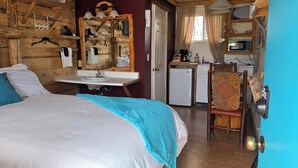 A cozy room with a large bed, a wooden headboard, a small sink, and a chair.