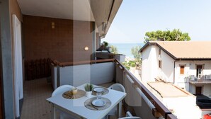 A balcony with a table set for two, overlooking a coastal area with buildings and trees. - Homiday - Lungomare dei Pini, D2 (Pineto)