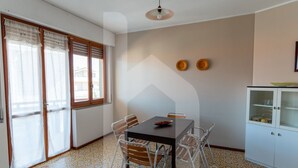 A dining area with a table and chairs, a cabinet with glass doors, and a window with curtains. - Homiday - Lungomare dei Pini, D2 (Pineto)