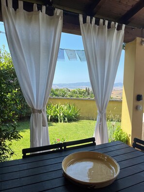 A table with a bowl and a chair, curtains, a view of greenery and hills, and a yellow wall. - La Casita de la Luz, deliziosa casa con vista sulla valle della Luce .... (Toscana)