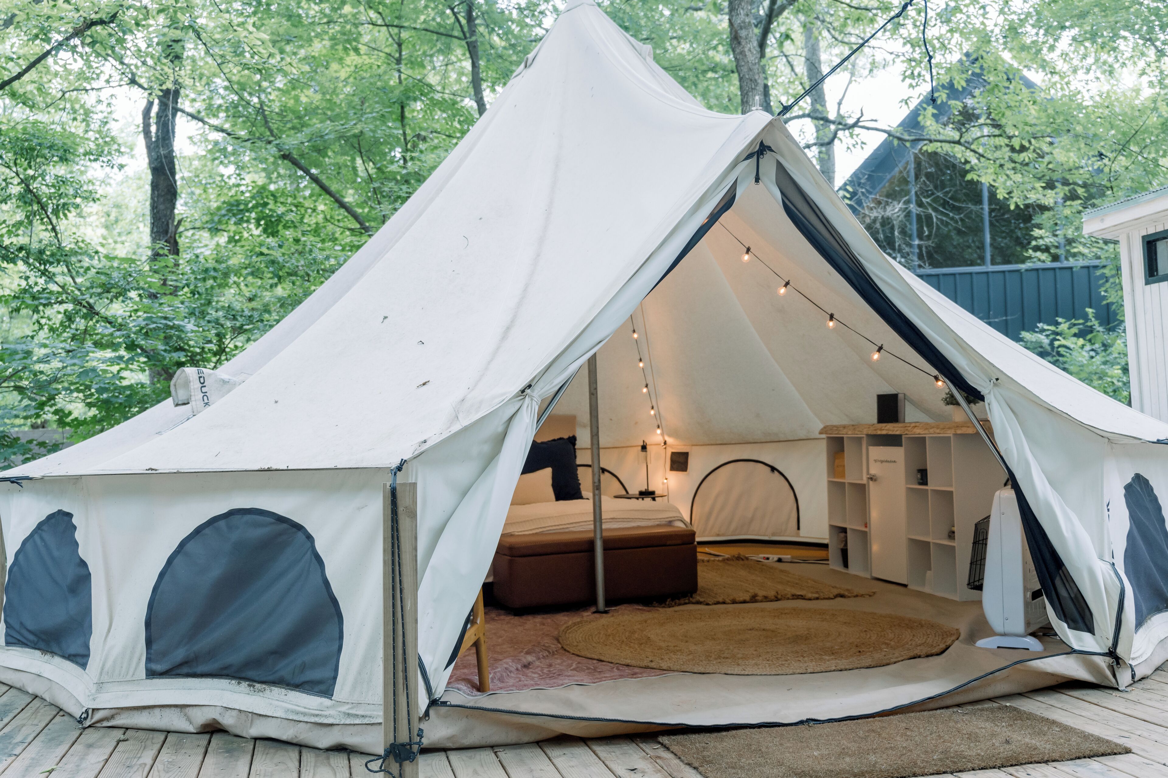 A tent with a bed, a small table, and a shelf unit inside.