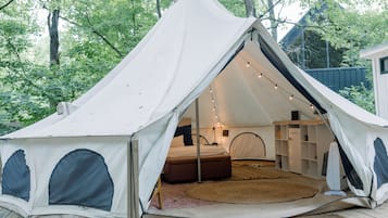 A tent with a bed, a small table, and a shelf unit inside.