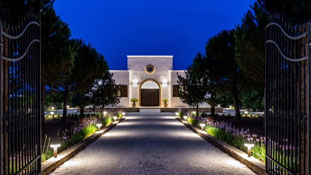 A gated entrance with a central archway, surrounded by well-lit pathways and flowering plants.