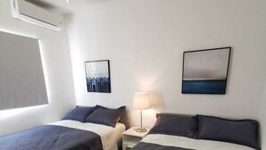 A hotel room with two beds, a nightstand, a lamp, and artwork on the walls.