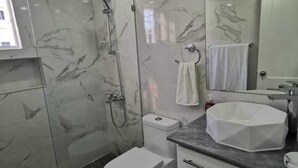 A modern bathroom with a glass-enclosed shower, a toilet, a sink with a marble countertop, and a large mirror.