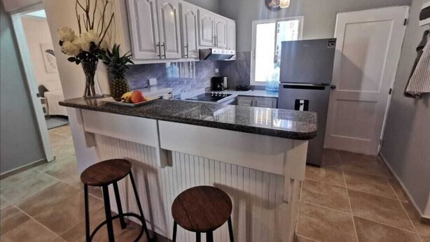A kitchen with white cabinets, a granite countertop, two stools, and a refrigerator.