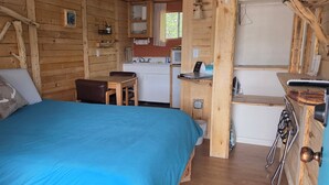 Ein rustikales Blockhaus-Interieur mit einem Bett, einer kleinen Küchenzeile und einem Essbereich aus Holz.
