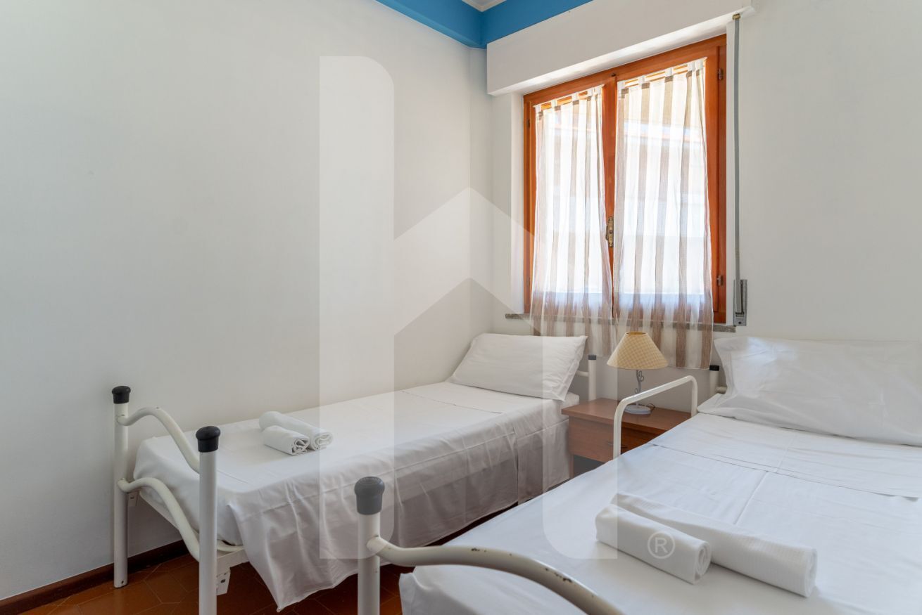 Una habitación de hospital con dos camas, una ventana con cortinas, una mesita de noche y una lámpara.