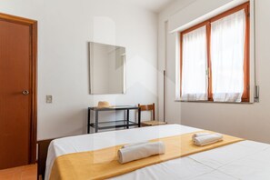 A hotel room with a bed, a desk, a chair, a window with curtains, and a door.
