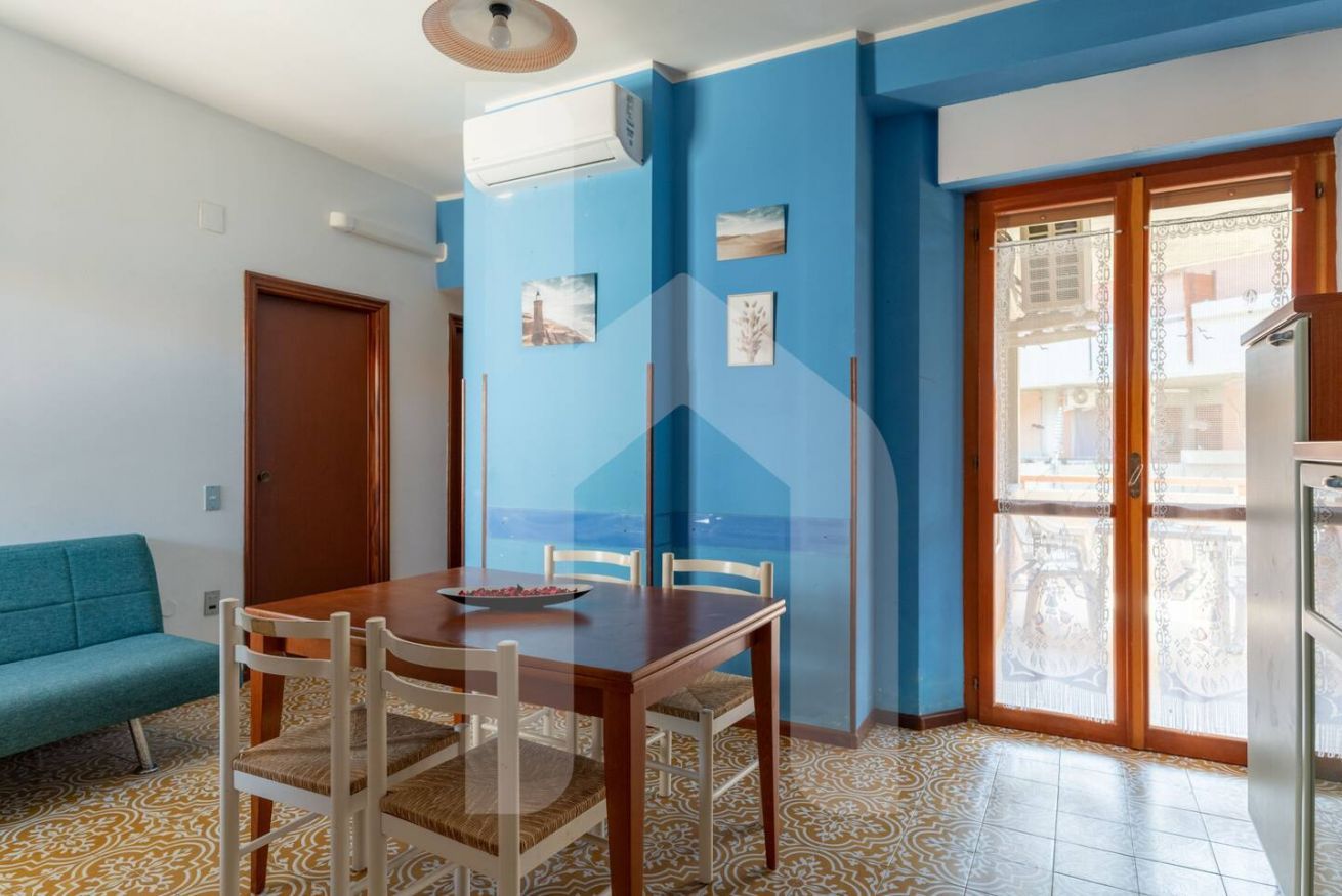A dining area with a wooden table and chairs, a blue wall, and a patterned floor.