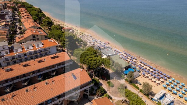 A coastal hotel with multiple floors, a beachside location, and numerous umbrellas along the shore. - Homiday - Waterfront of the Pines, D1 (Pineto)