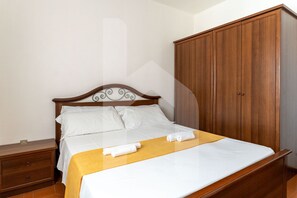 A neatly made bed with white linens and a wooden headboard, a wooden wardrobe, and a small wooden nightstand with drawers. - Homiday - Waterfront of the Pines, D1 (Pineto)