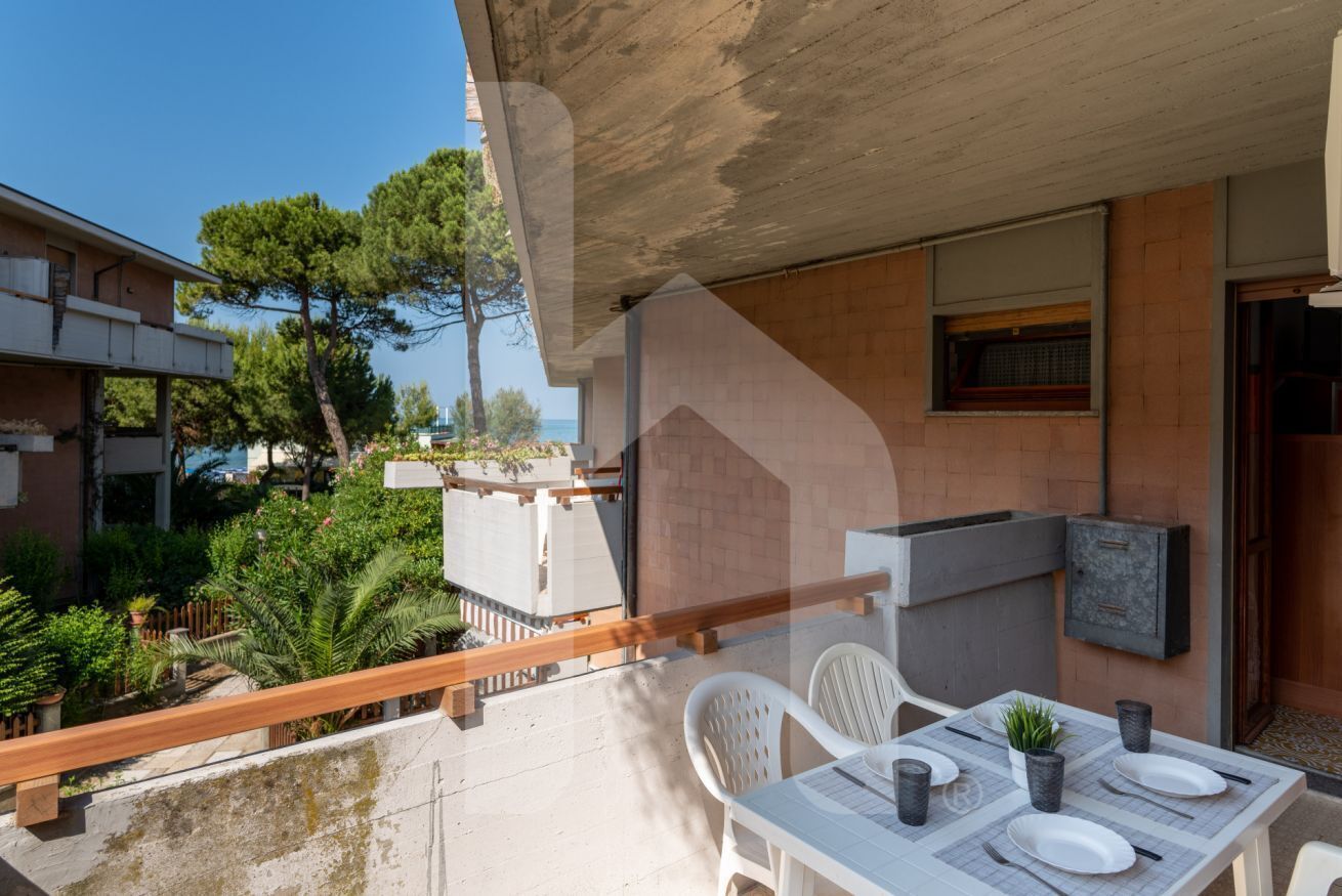 A balcony with a table set for two, a grill, and a view of the sea.