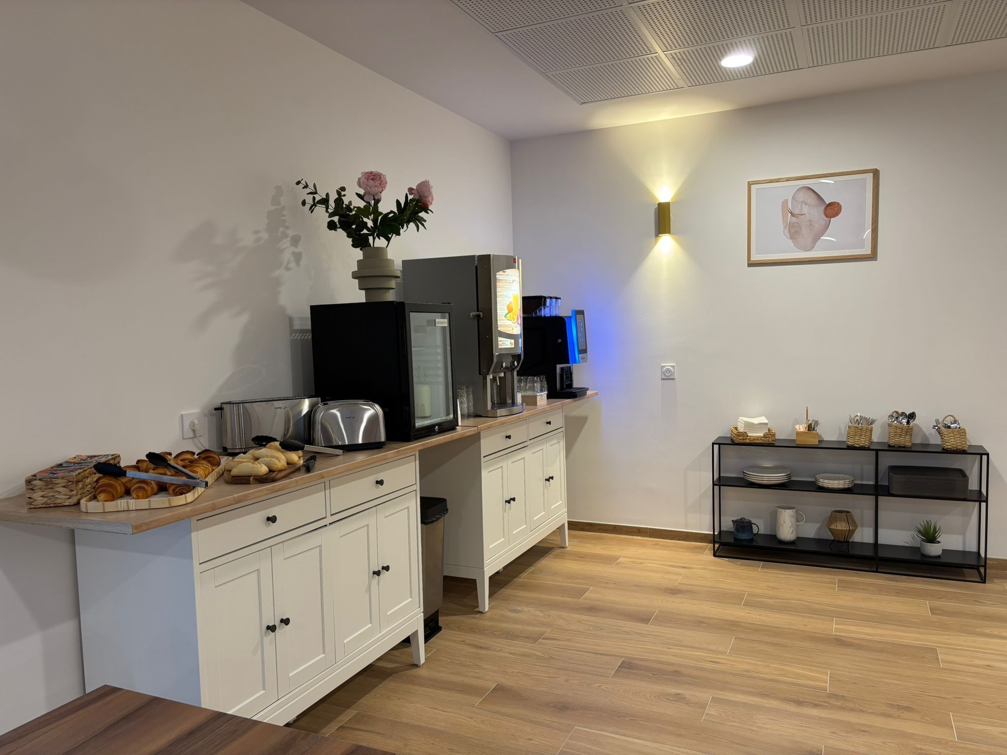 A modern kitchen with white cabinetry, a wooden countertop, a coffee machine, a refrigerator, and a wall-mounted light.