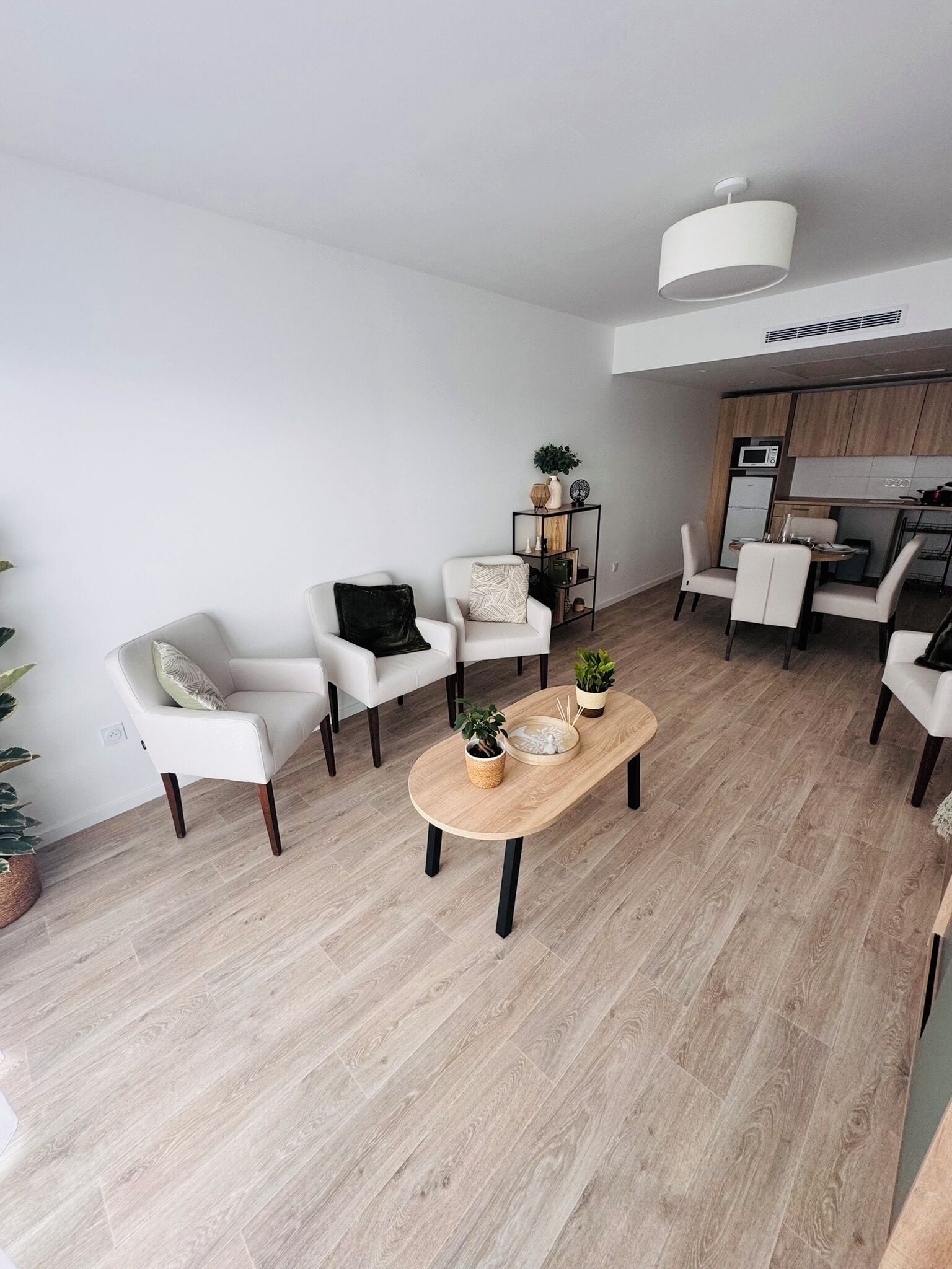 Un salon moderne avec une table basse en bois, des canapés blancs et un petit coin cuisine équipé d’un four à micro-ondes et d’un réfrigérateur.