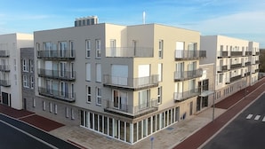 Un immeuble résidentiel moderne à plusieurs étages, doté de balcons, de grandes fenêtres et d’un trottoir rouge.