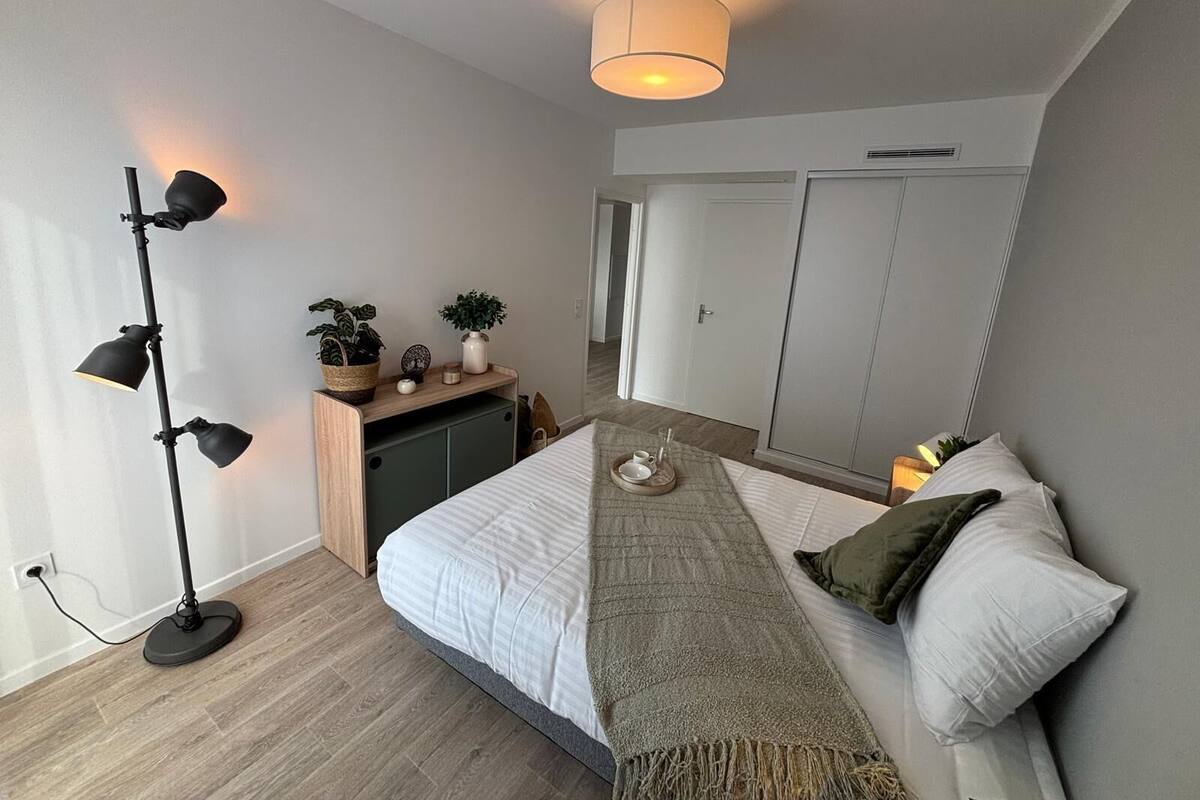 Een slaapkamer met een bed, nachtkastje, lamp, kledingkast en uitzicht op de gang.
